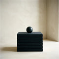 Stack of five black cloth-bound books with a stone sphere on top, on ivory plaster
