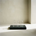 Three empty glass vials in a row on a black stone tray, on ivory plaster