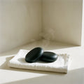 Two black basalt stones on a folded white linen towel, on ivory plaster